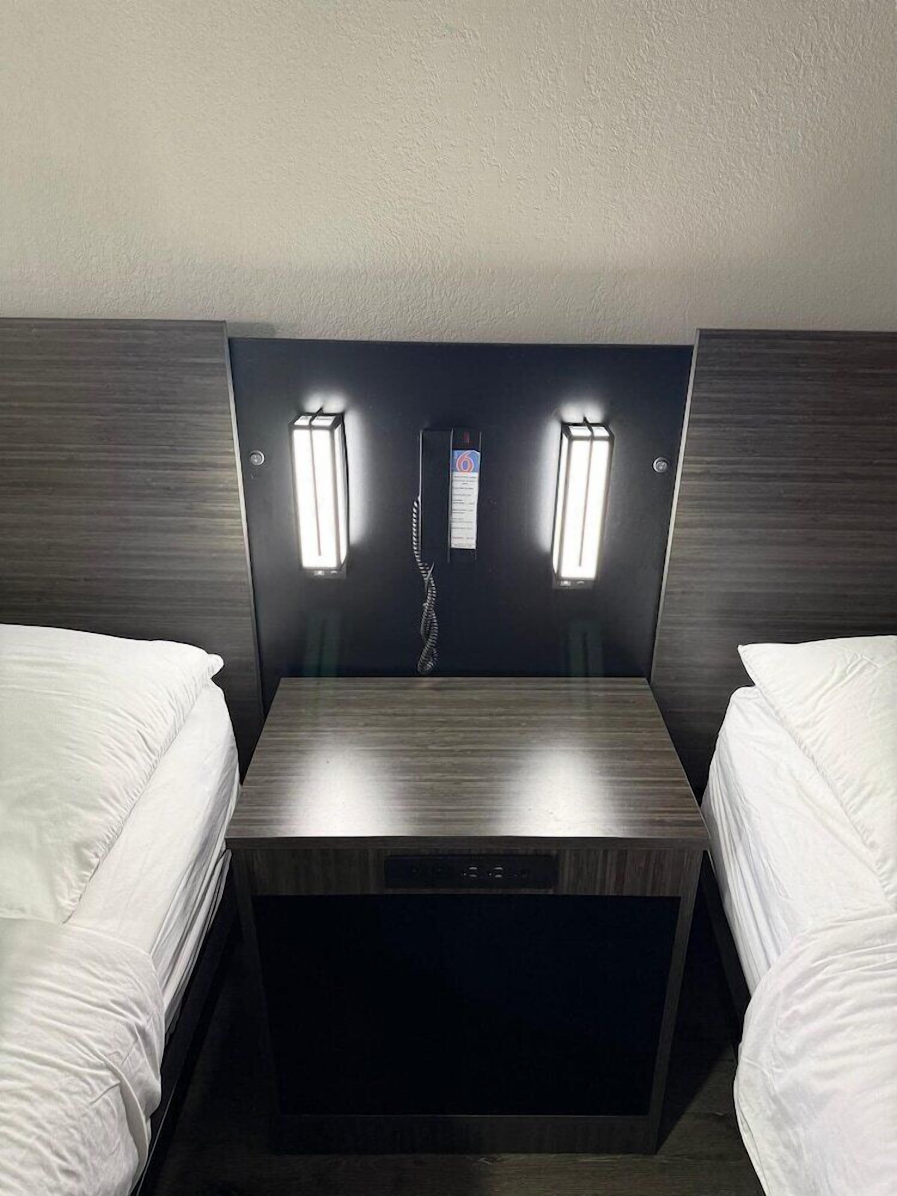 A hotel room with two single beds, a small table, and a wall-mounted telephone.