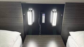 A hotel room with two single beds, a small table, and a wall-mounted telephone.