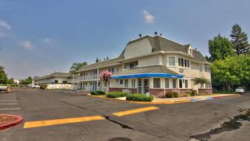 A motel with a central building and two wings, featuring a blue awning and a 'Welcome' sign.
