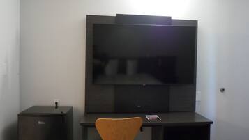 A room with a flat-screen TV mounted on the wall, a wooden chair, and a small cabinet.