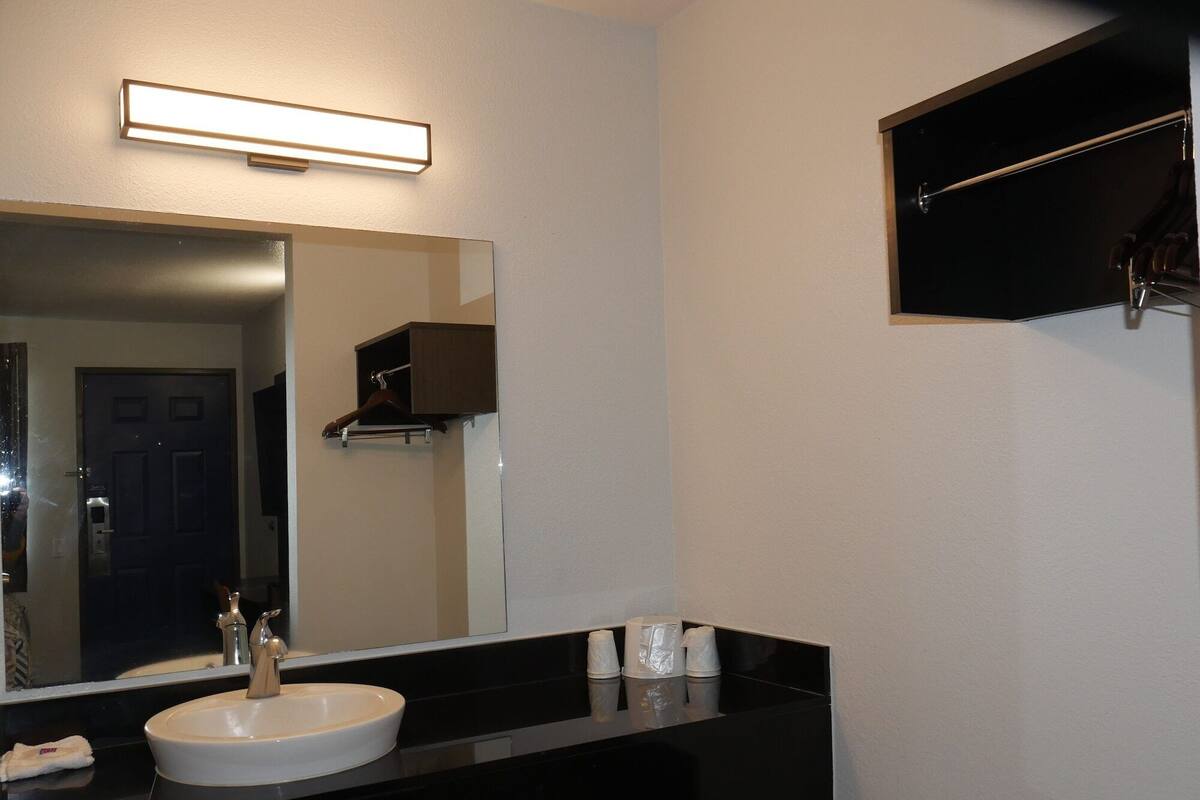A modern bathroom with a black countertop, a white sink, a large mirror, and a towel rack.