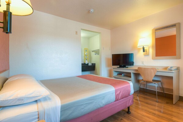Ein Hotelzimmer mit einem Bett, einem Schreibtisch, einem Sessel, einem Fernseher und einem Spiegel.