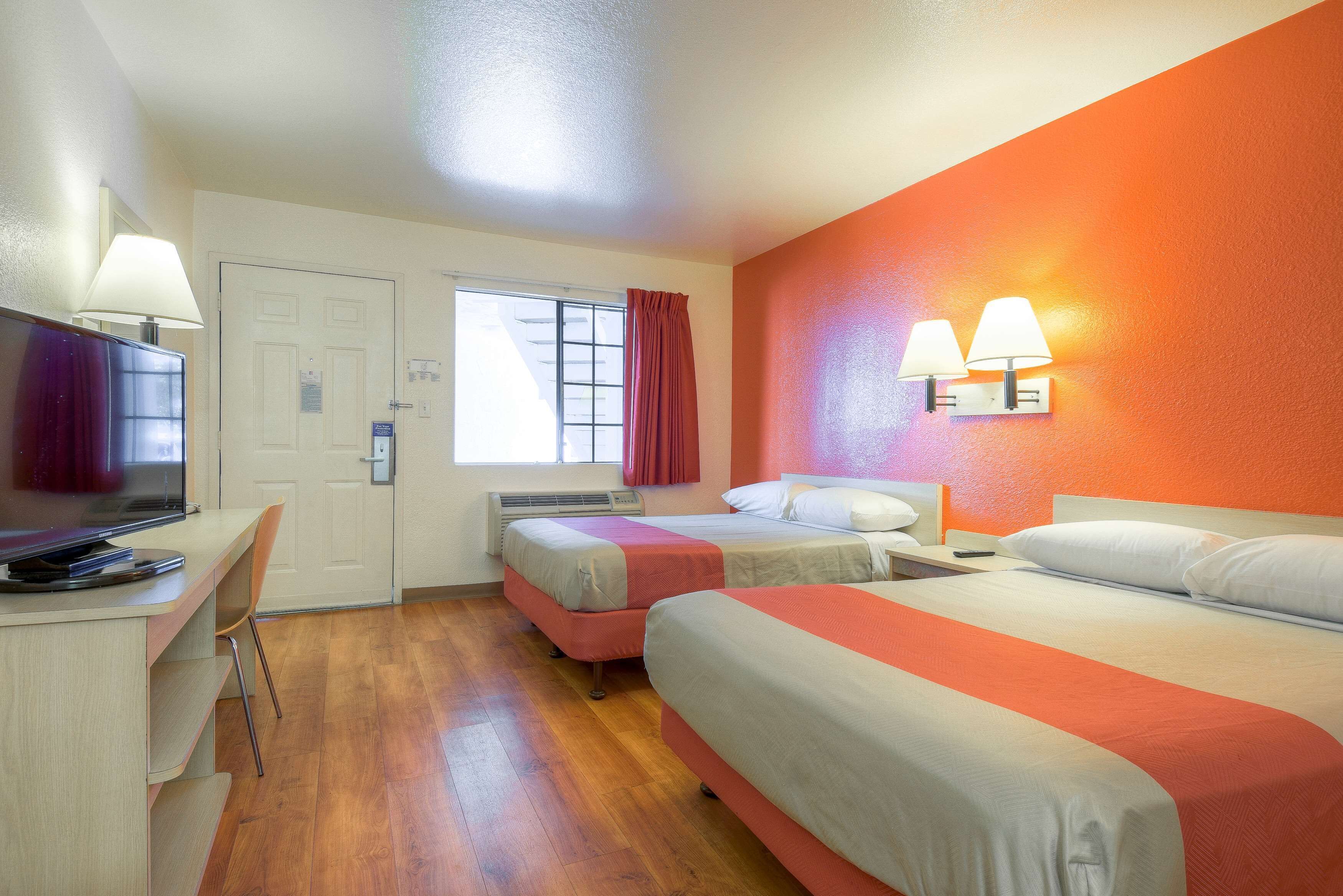 A hotel room with two beds, a desk with a computer, a television, and two wall-mounted lamps.