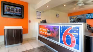 A hotel reception area with a digital screen displaying weather information, a large illuminated number '6', and a sign promoting the hotel.