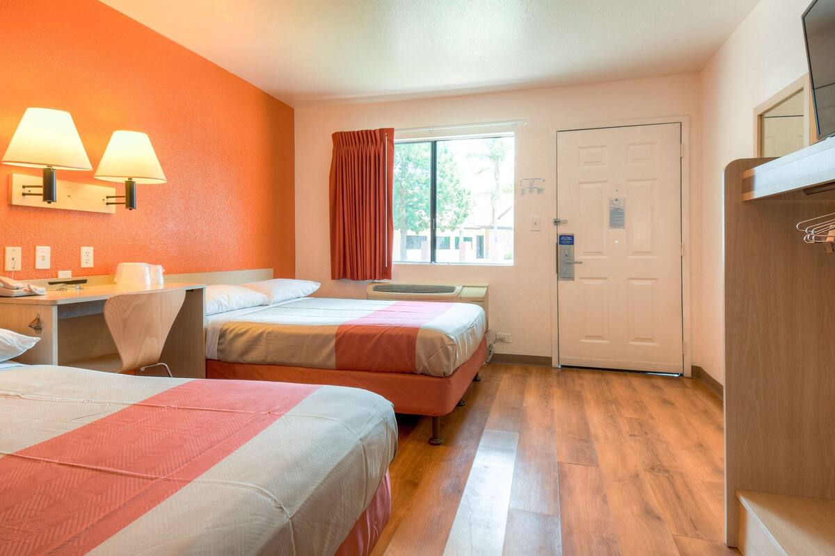 A hotel room with two beds, a desk, a chair, a window with curtains, a door, and a wardrobe.