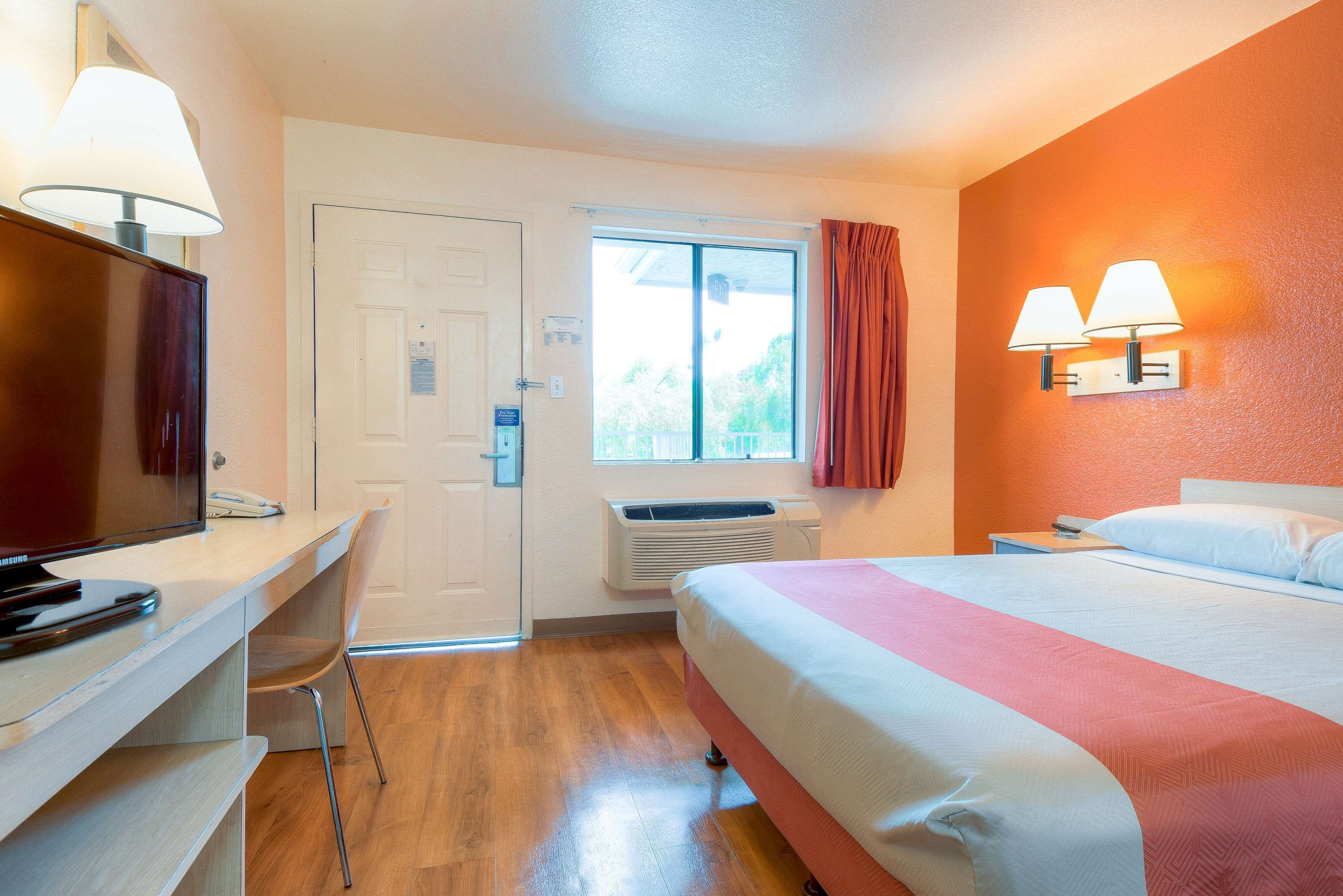 Ein Hotelzimmer mit Bett, Schreibtisch, Fernseher und einem Fenster mit Vorhängen.
