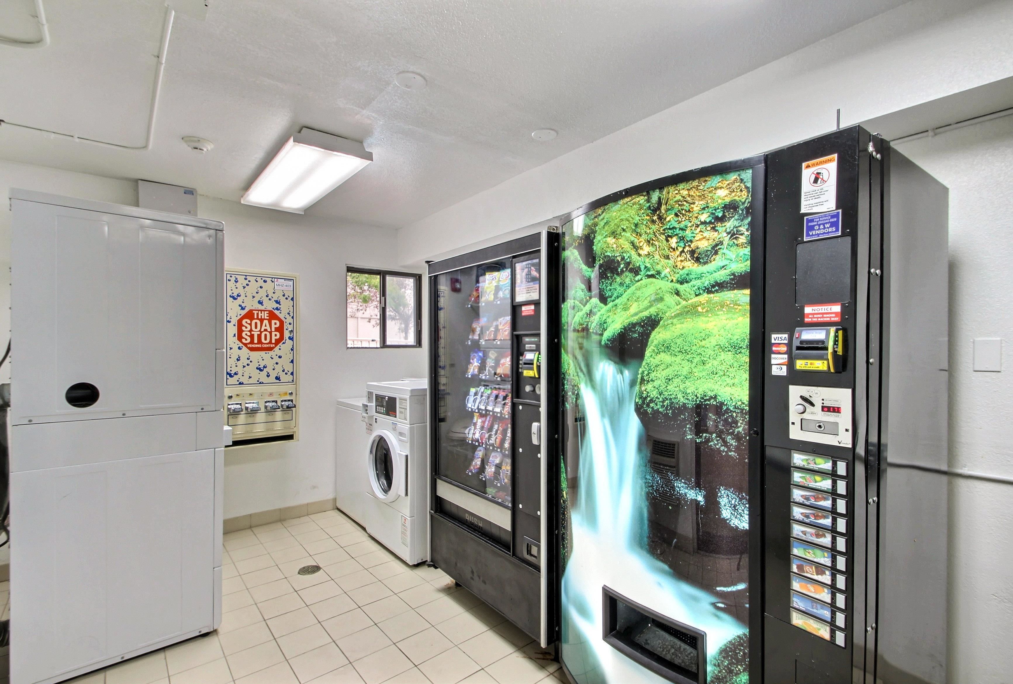 A laundry room with a washing machine, dryer, and a vending machine with a waterfall display.
