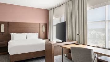 A hotel room with a bed, a desk, a chair, a TV, and a large window with curtains.