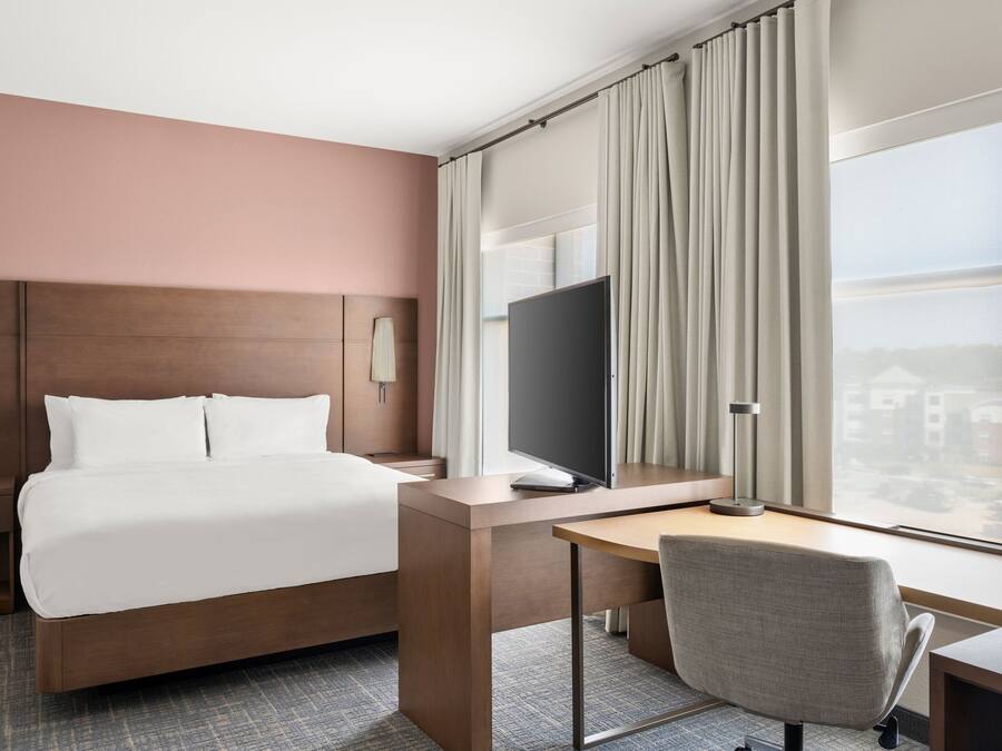 A hotel room with a bed, a desk, a chair, a TV, and a large window with curtains.