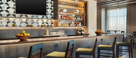 Zona de bar con diseño moderno, destacando un backsplash de azulejos geométricos, un televisor de pantalla plana y una variedad de botellas y vasos en estantes.