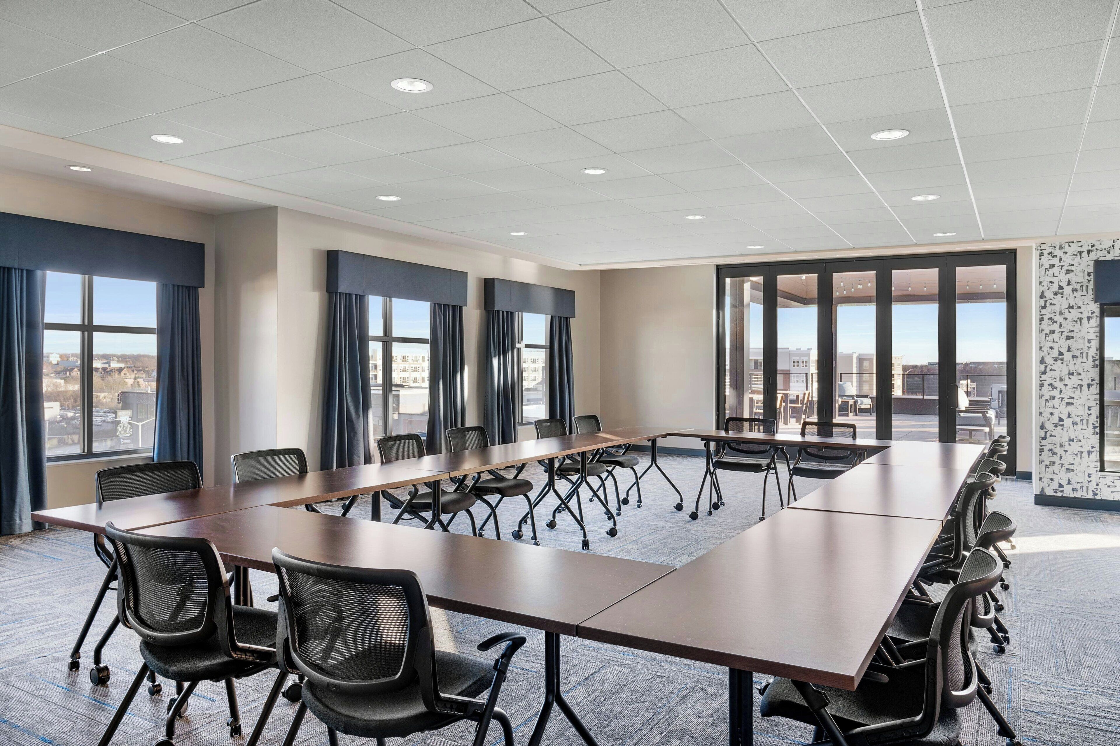 A conference room with a long table, multiple chairs, and large windows offering a city view.
