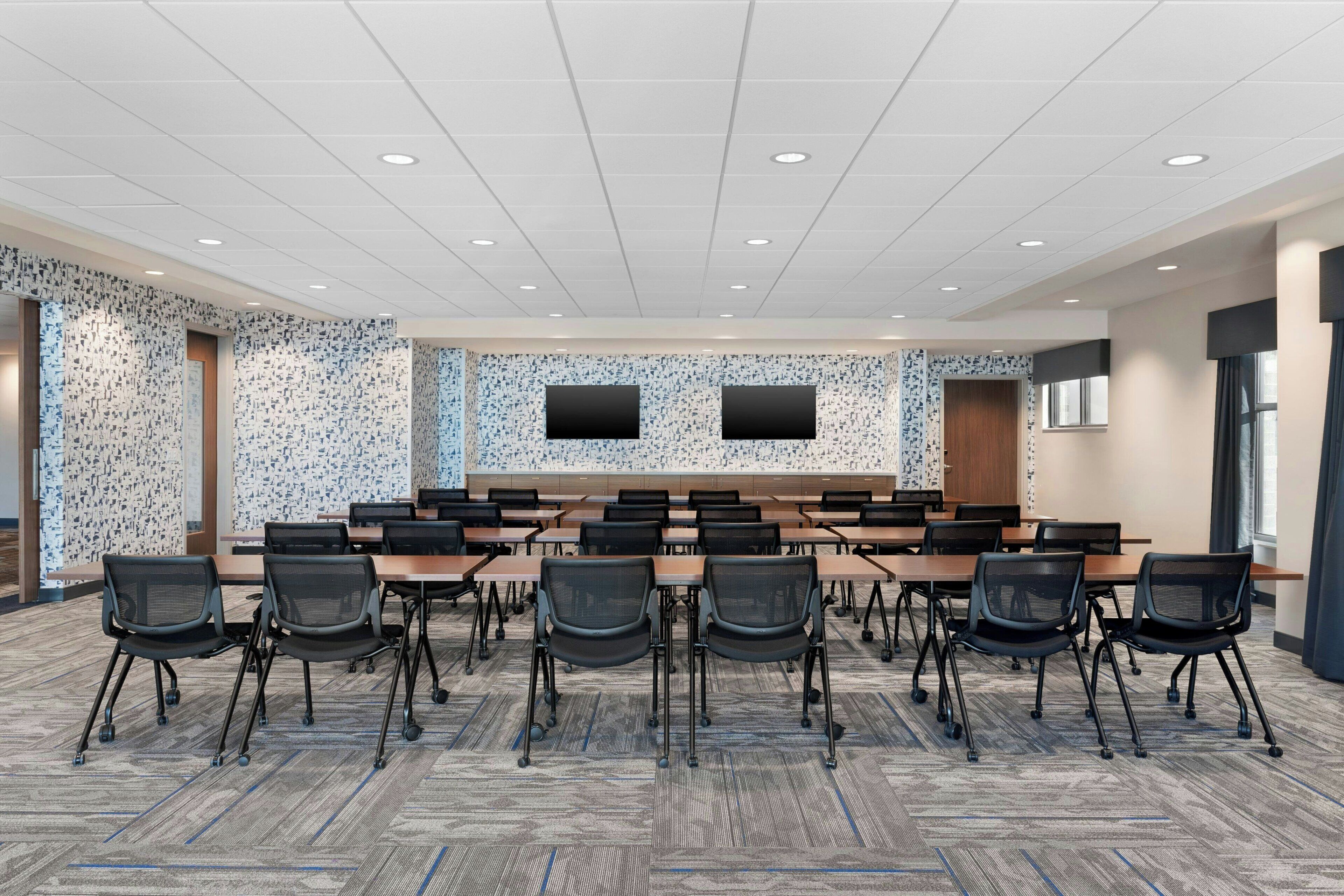 A conference room with a long table, multiple chairs, and two screens on the wall.