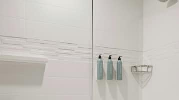 A modern bathroom with white tiles, a glass shower enclosure, and a towel rack with three bottles.