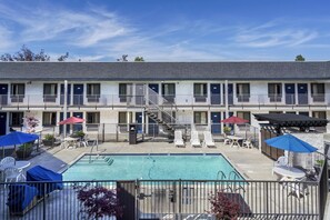 A motel with a pool area, outdoor seating, and a staircase leading to the upper floor.