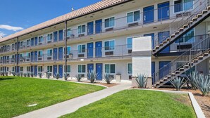 A multi-story motel with a central walkway, blue doors, and a staircase on the right. - Motel 6 Escondido, CA (Escondido)