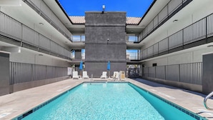 A swimming pool with clear water, surrounded by a building with balconies and a tiled floor. - Motel 6 Escondido, CA (Escondido)