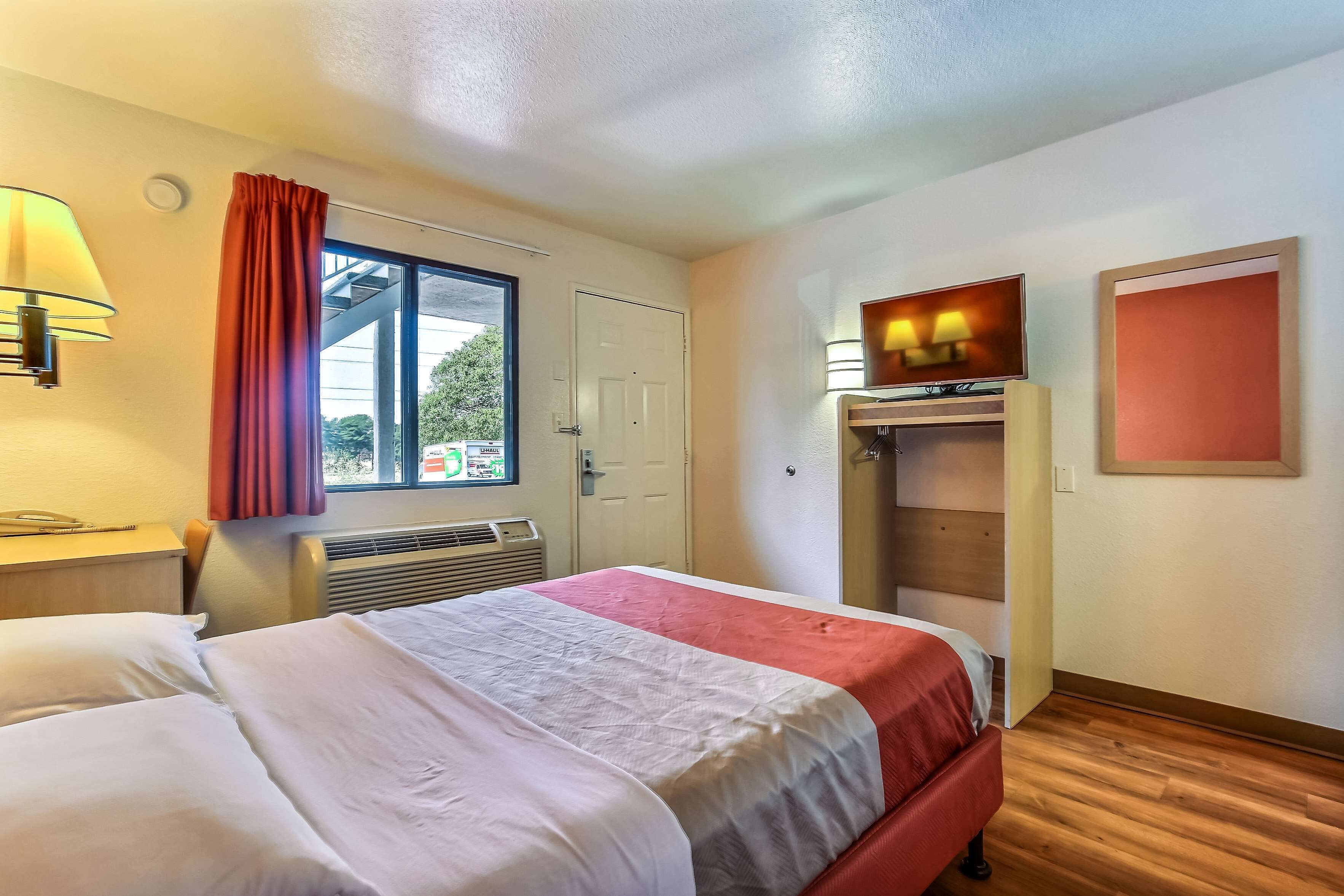 Une chambre d’hôtel avec un lit, une fenêtre avec des rideaux, un radiateur, une télévision et une armoire.