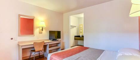A hotel room with a bed, a desk, a chair, a television, and a bathroom visible through an open door.