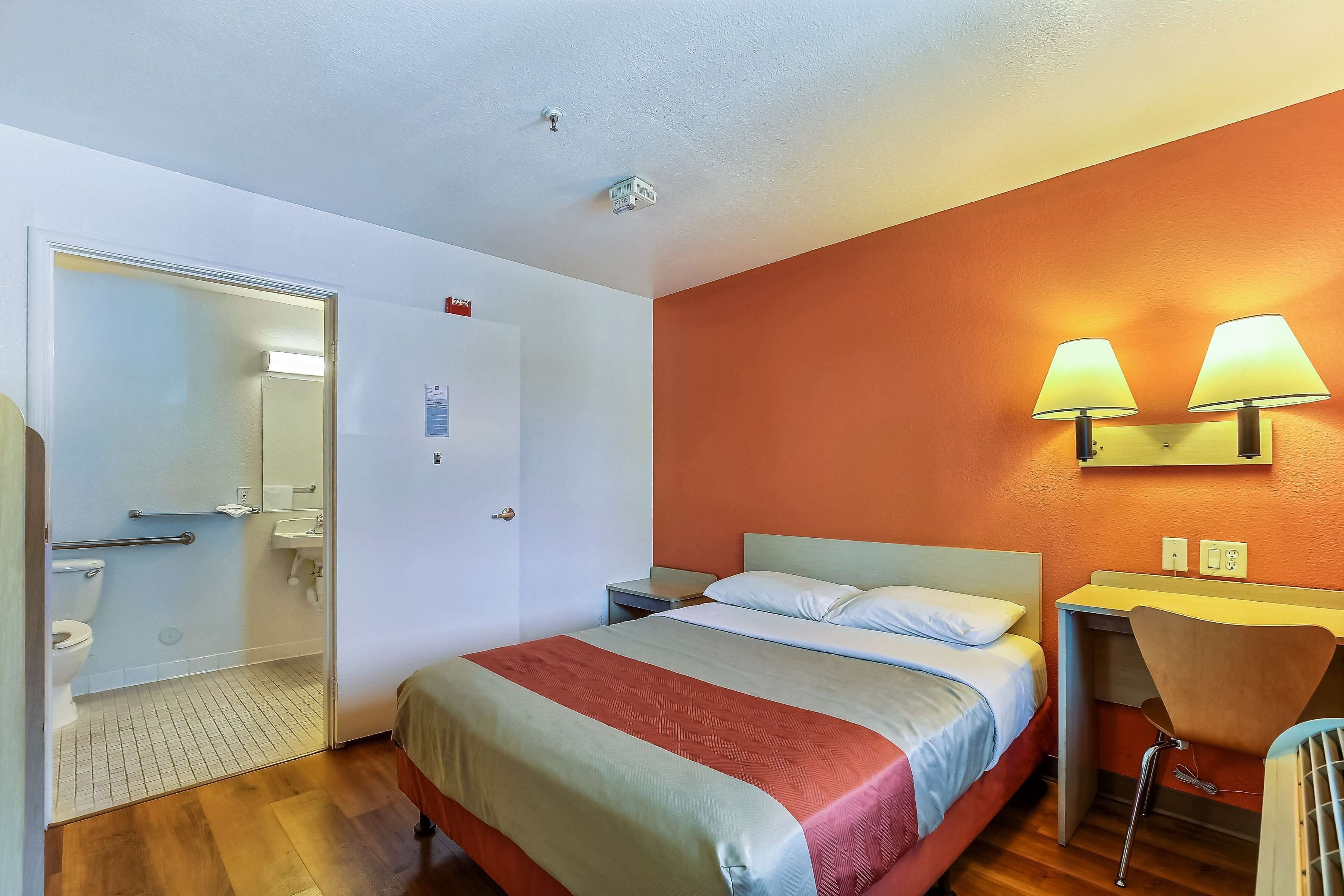 A hotel room with a bed, bedside table, chair, and a small desk area.