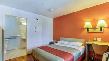 A hotel room with a bed, bedside table, chair, and a small desk area.