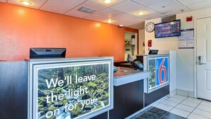 A motel reception desk with a sign that reads "We'll leave the light on for you." - Motel 6 Pinole, CA (Pinole)