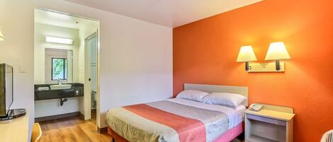 Un dormitorio con cama, mesita de noche, lámpara y vistas al baño.
