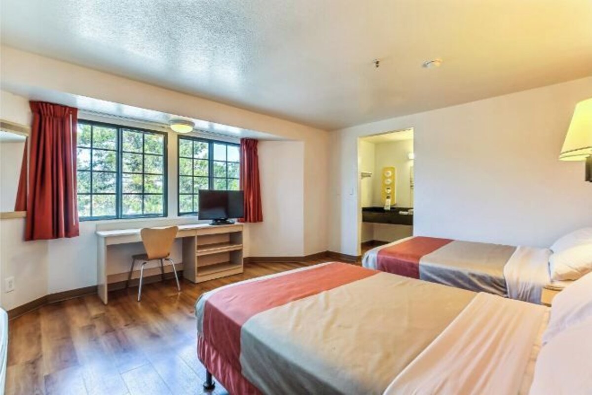A hotel room with two beds, a desk, a chair, and a television.