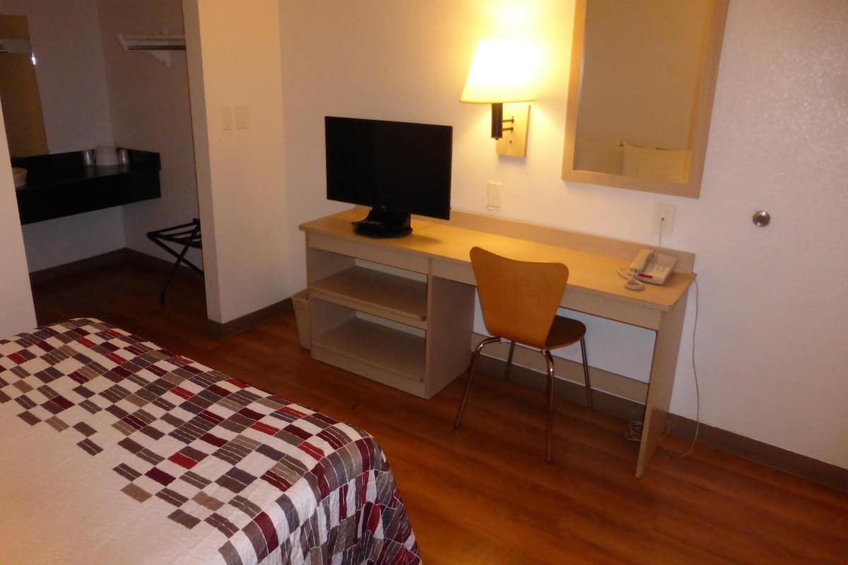 Habitación de hotel con cama, escritorio con televisor, silla, lámpara de escritorio, teléfono y espejo.
