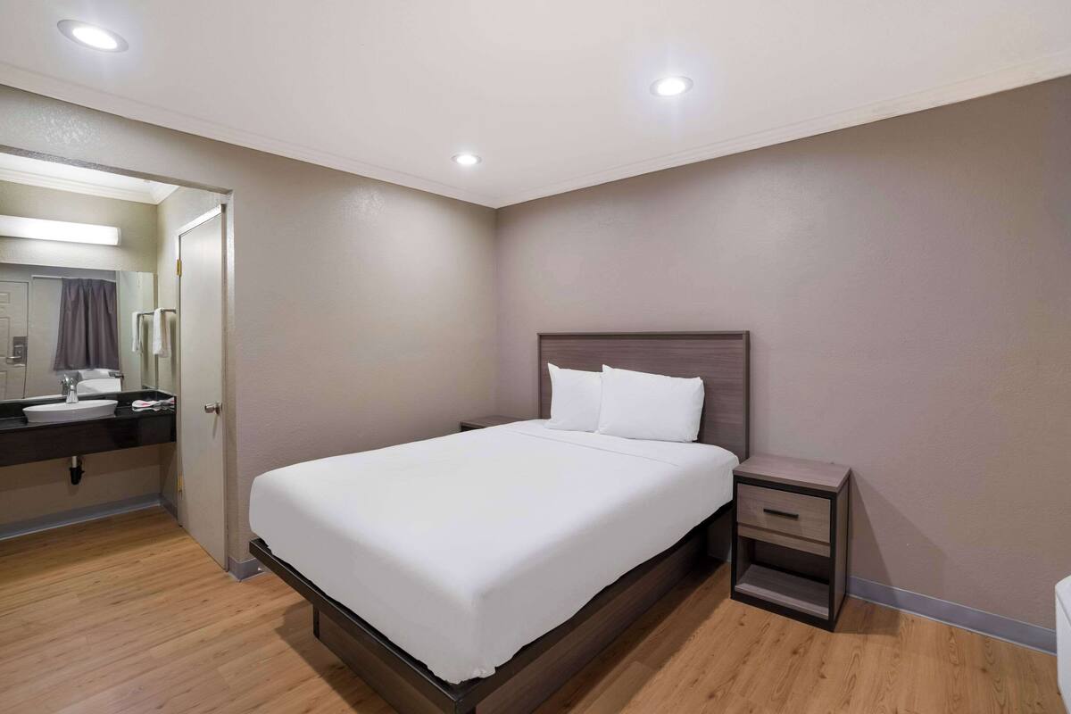 A neatly arranged bedroom with a bed, bedside table, and a bathroom visible through an open door.