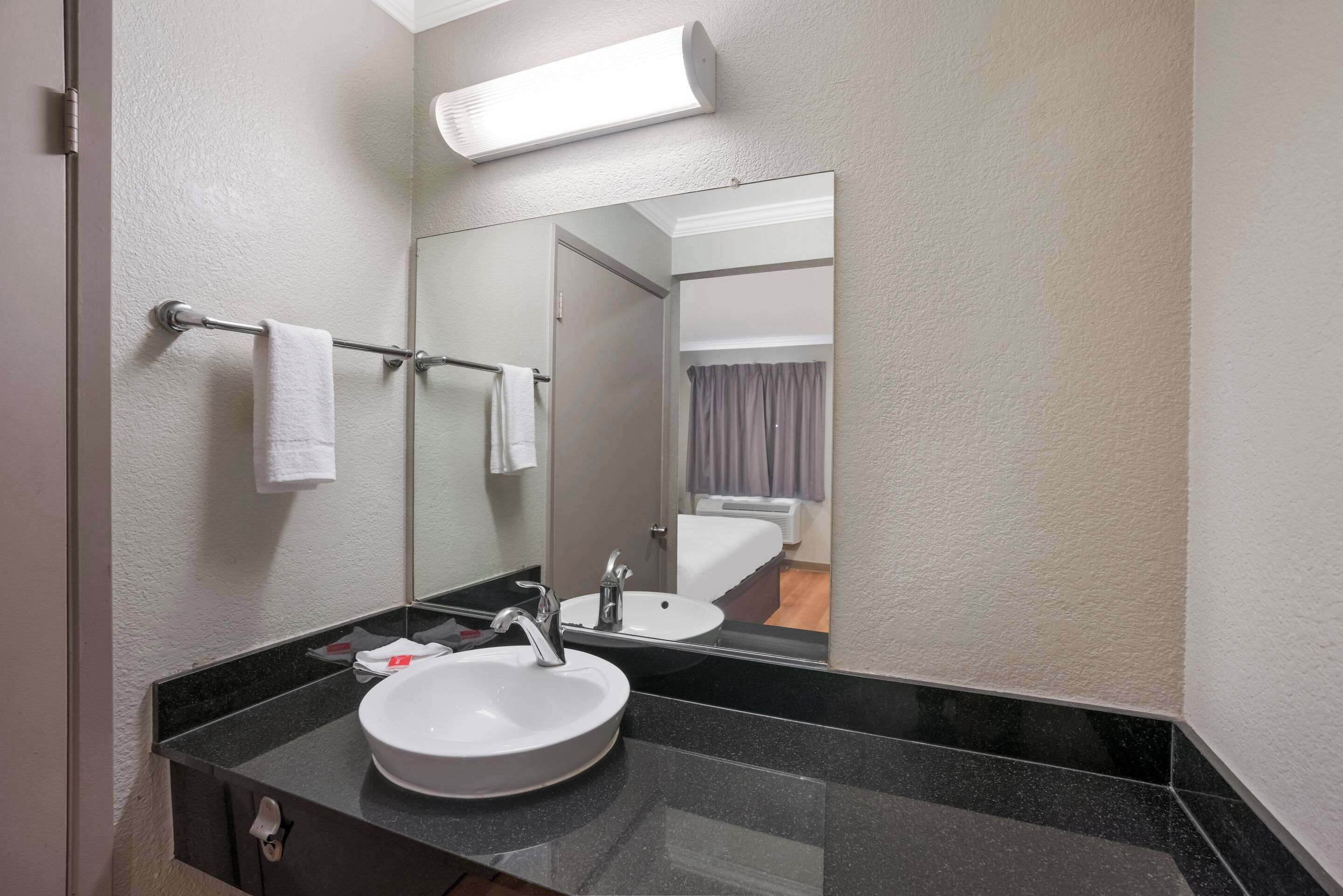 Un baño con un lavamanos blanco, un espejo y un perchero para toallas.