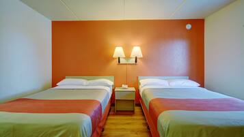 A hotel room with two single beds, a nightstand with a lamp, and an orange accent wall.