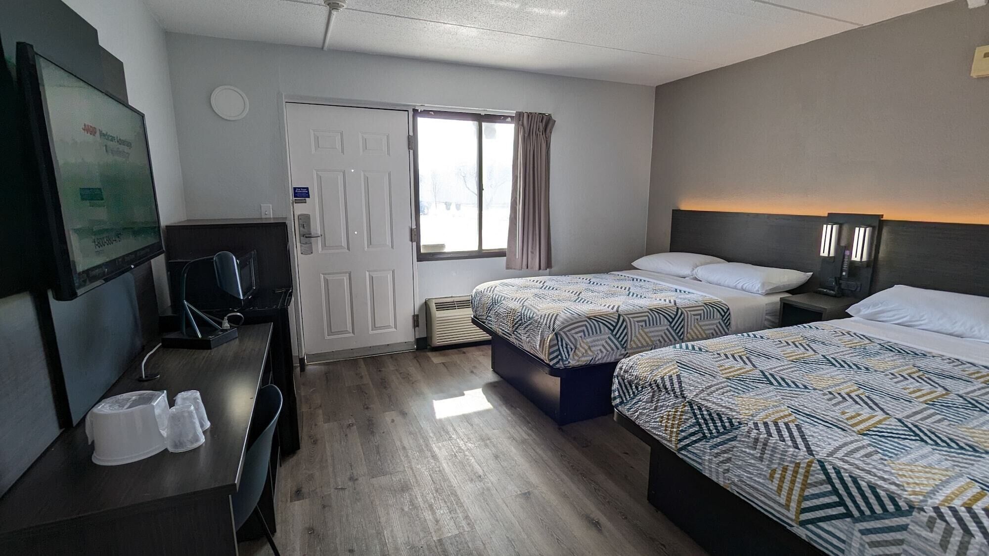 A hotel room with two beds, a desk with a computer, a TV, and a window with curtains.