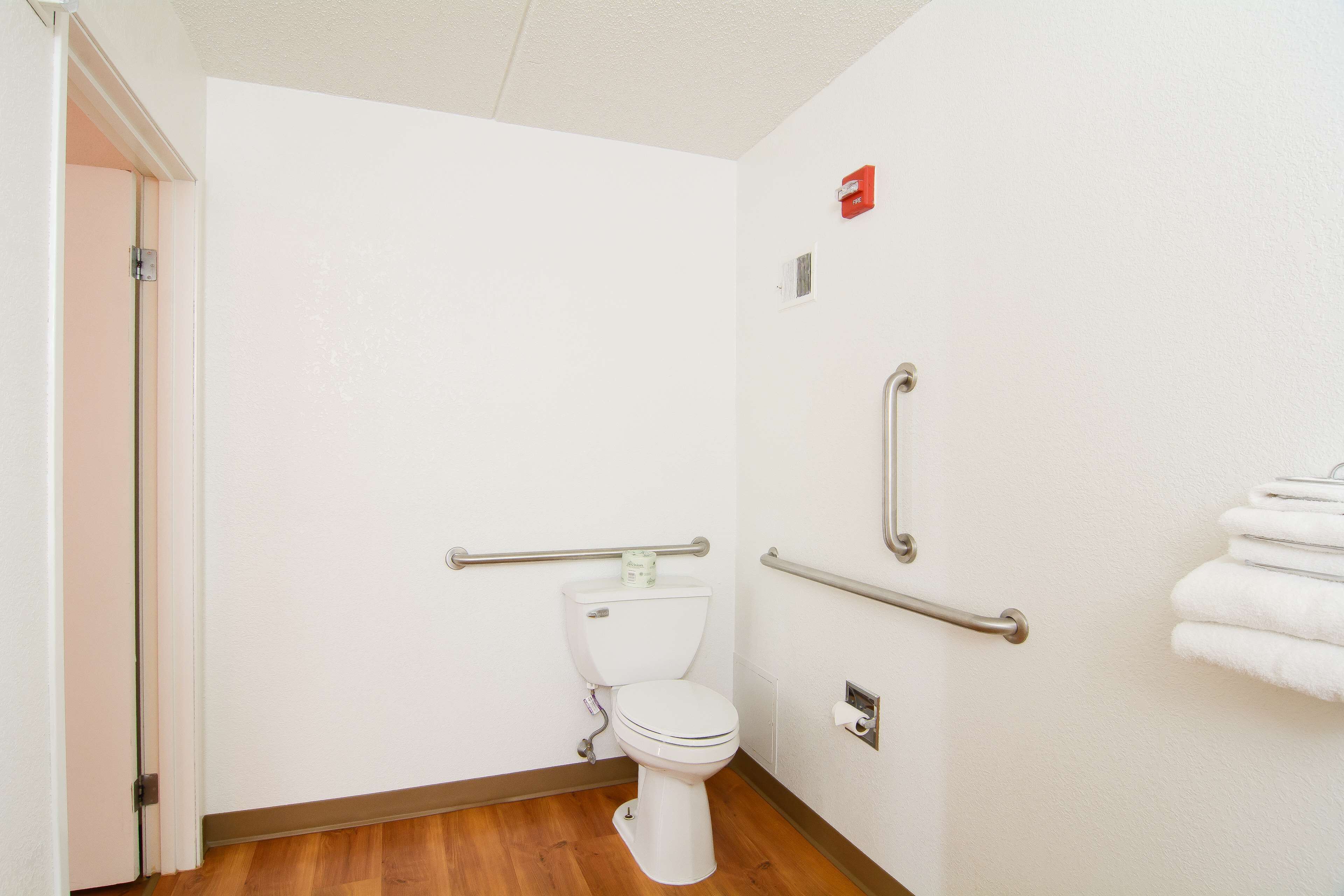 A small, clean bathroom with a white toilet, handrails, and a towel rack.