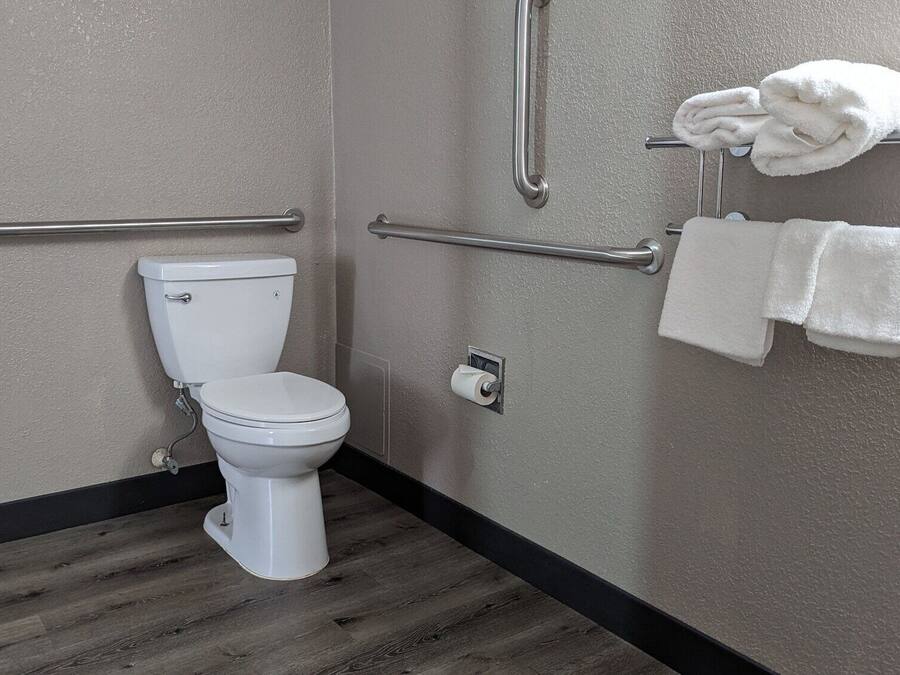 A bathroom with a toilet, grab bars, and a towel rack with towels.