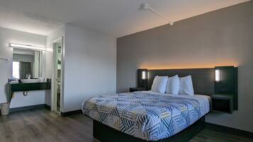 Habitación de hotel con una cama grande, una mesita de noche, un tocador y un baño con lavabo y toallero.