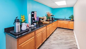 A kitchen with wooden cabinets, a black countertop, and a teal wall. - Howard Johnson by Wyndham Houston Hobby Airport (Houston)