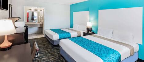 A hotel room with two beds, a desk with a lamp, a mirror, and a bathroom with a sink and mirror.