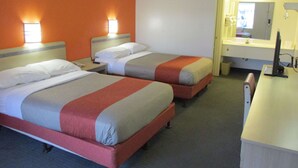 Quarto de hotel com duas camas, uma escrivaninha, uma cadeira, um espelho e banheiro com pia e vaso sanitário.