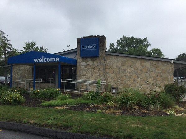 L’entrée d’un hôtel Travelodge, avec une pancarte « Bienvenue », une façade en pierre et un espace d’entrée abrité.