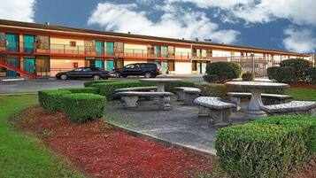 A motel with a parking lot, outdoor seating area, and a building with multiple balconies.