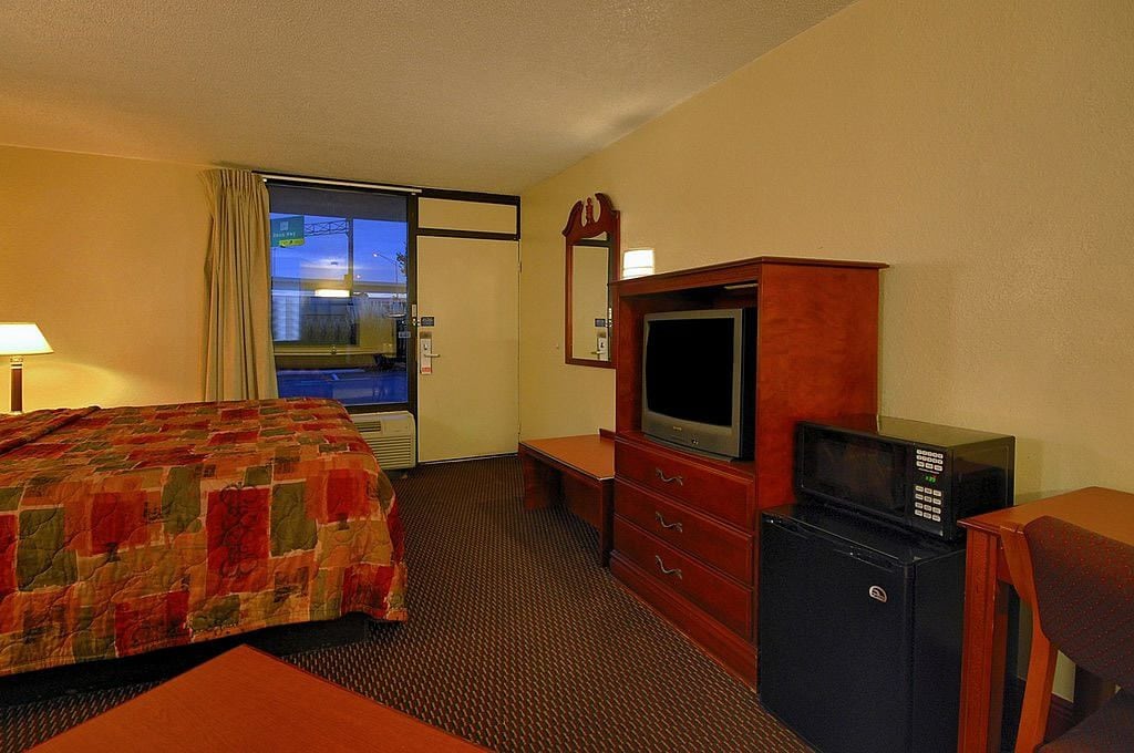 A hotel room with a bed, a TV, a microwave, and a dresser.