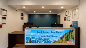 Un mostrador de recepción con una pantalla grande mostrando un paisaje de montaña y un mensaje promocional.