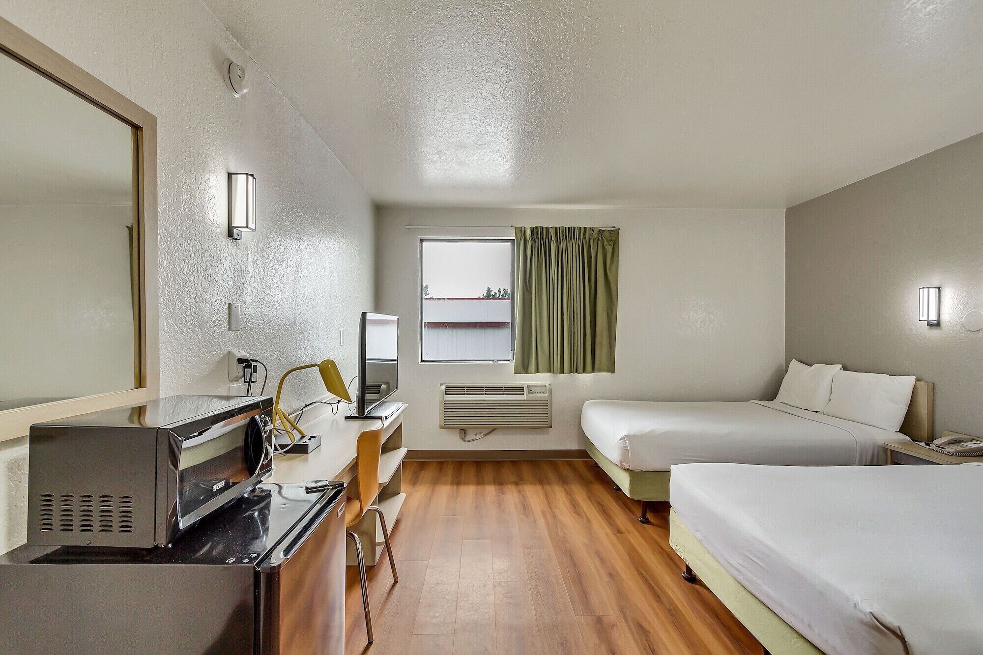 A hotel room with a desk, computer, two beds, a mirror, and a window with curtains.