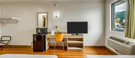 A hotel room with a bed, a desk with a computer, a microwave, a chair, and a window with a view of the outside.