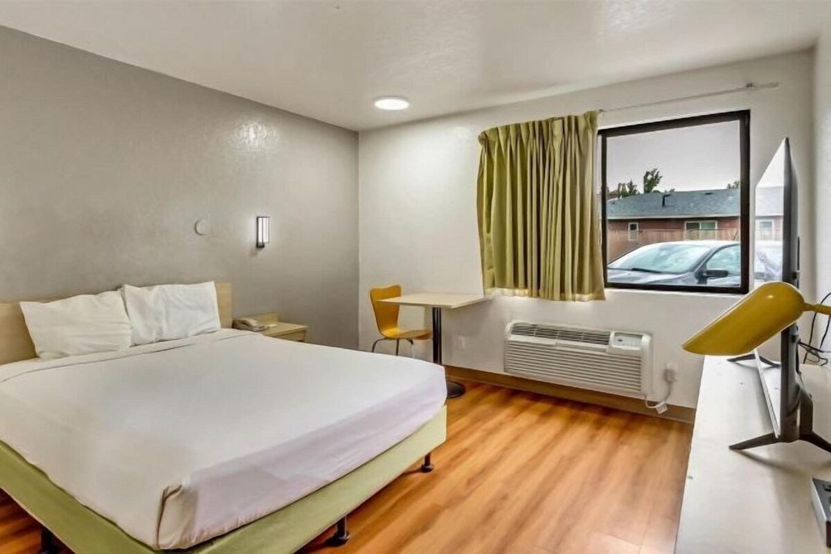 A hotel room with a bed, a desk, a chair, a window with curtains, and a radiator.