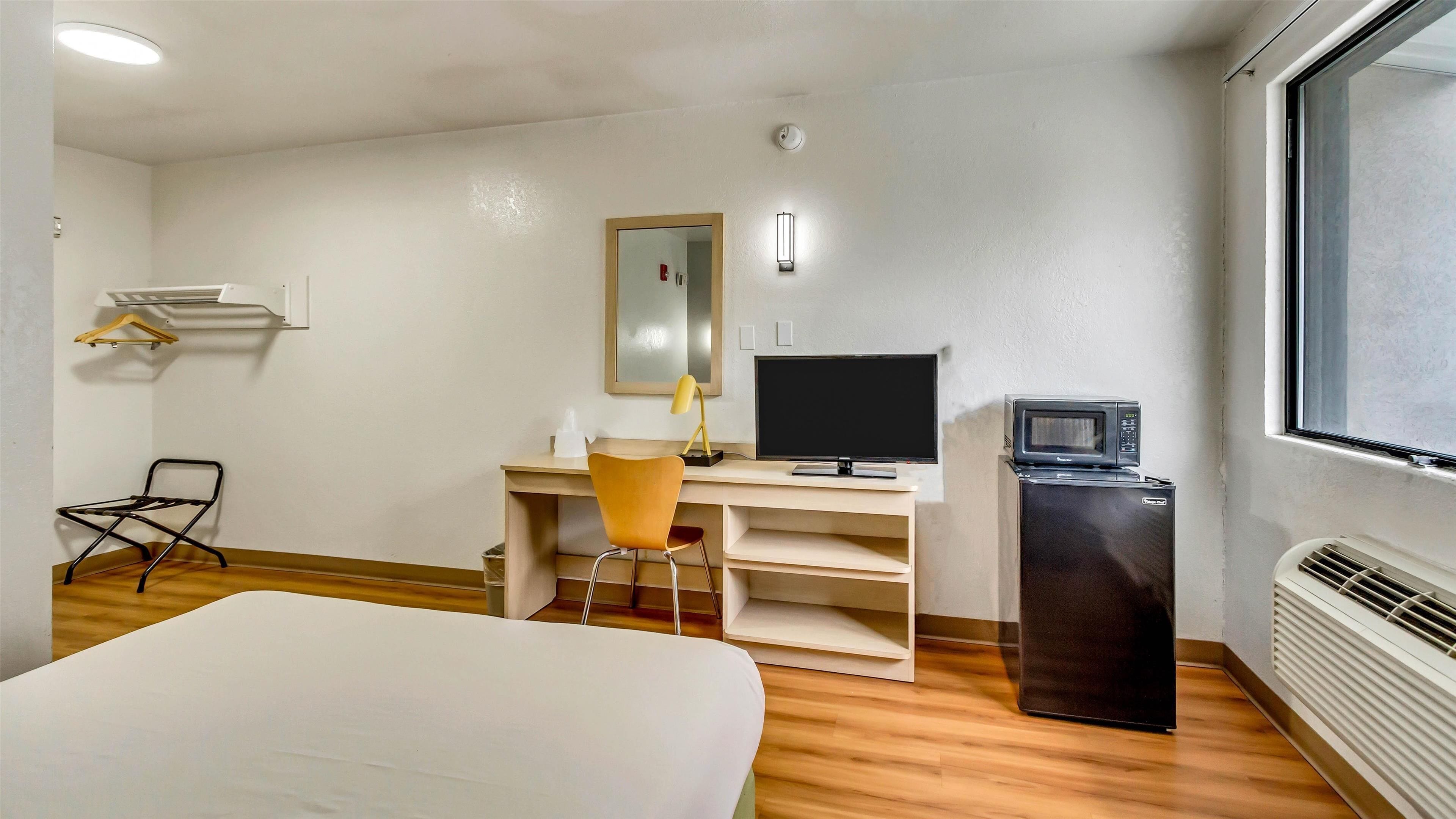 A hotel room with a bed, a desk with a computer, a chair, a TV, a microwave, and a heater.