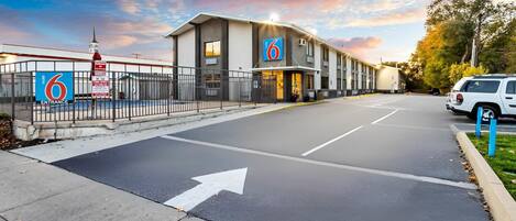 A motel with a gated entrance, a clear road with directional arrows, and a white SUV parked nearby.