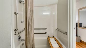 A bathroom with a shower, grab bars, a towel rack, and a small wooden bench.