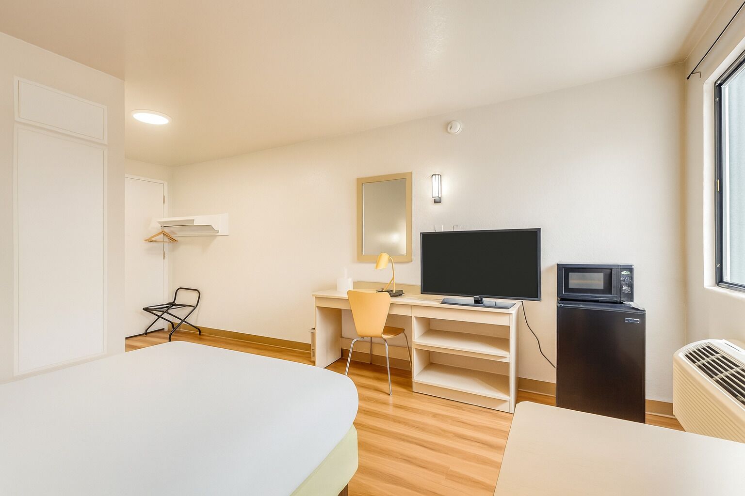 A hotel room with a bed, a desk with a computer, a TV, a microwave, and a window.