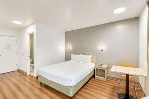 Quarto de hotel com cama, mesa de cabeceira, luminária e uma pequena mesa com cadeira.